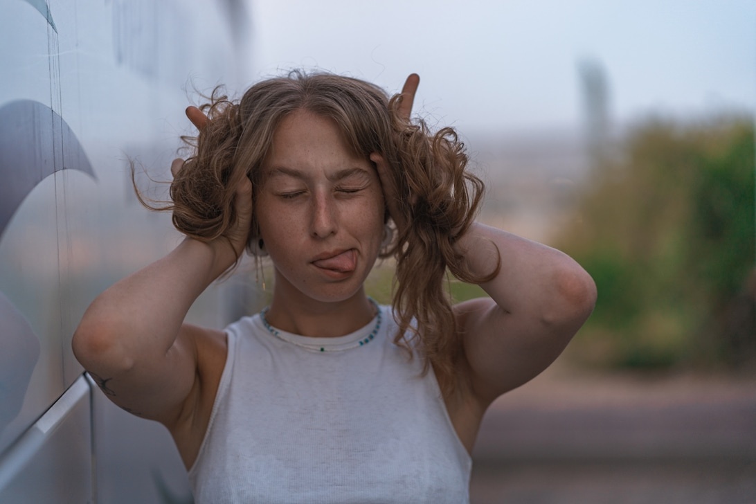 En ung kvinna med ett frustrerat ansiktsuttryck som drar händerna genom sitt hår, vilket symboliserar den psykiska påfrestningen av stress.
