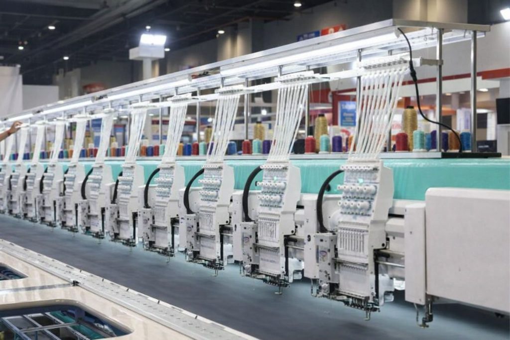 Rad av industriella broderimaskiner med trådar i flera färger, redo för tryck på tyg.